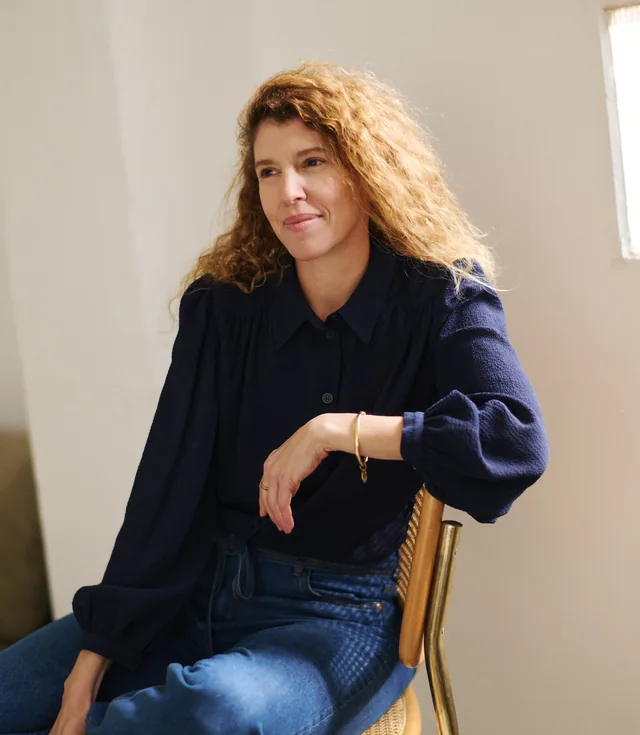 Ximena Roe, seated on a cane chair by a window, in a navy shirt and jeans
